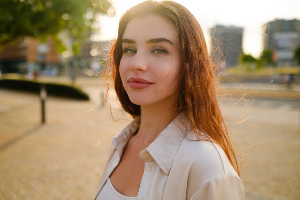 Mysterious red haired girl stands in the park at sunset.