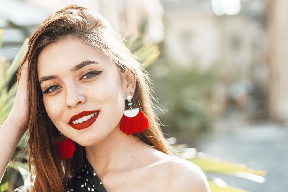 Outdoor close up portrait of yong beautiful happy smiling woman with red lips, long hair, wearing long tassel earrings. Summer fashion concept. Copy, empty space for text