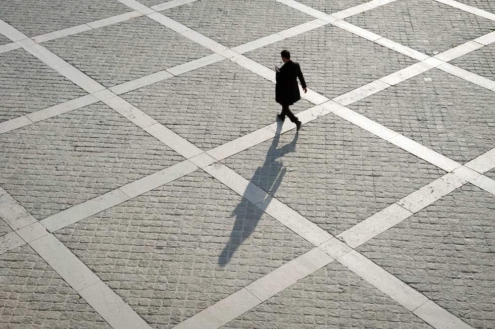 Overhead view of unrecognizable pedestrian casting shadow on the geometric patterns of a stone plaza on a quay next to the River Seine in Paris, France