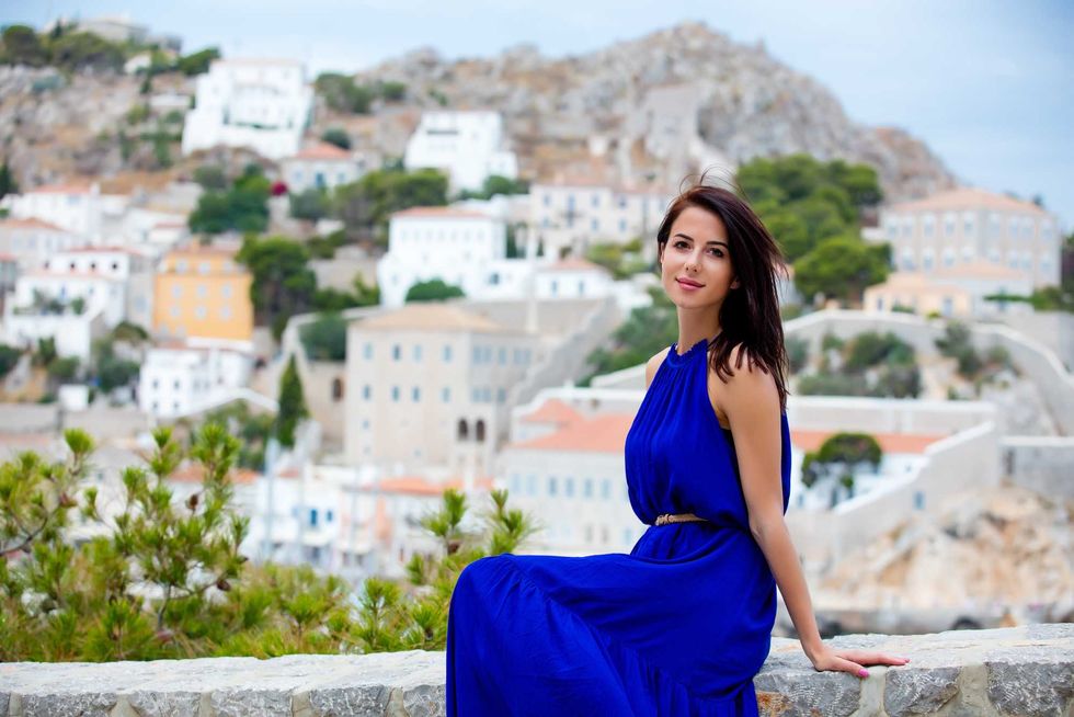 photo of beautiful young woman sitting on the stairs on the town background in Greece
