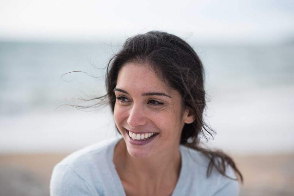 Portrait of a beautiful young brunette woman on the beach, she has long hair and wears a sweater