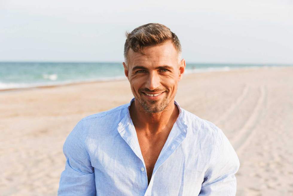 Portrait of a handsome smiling man in shirt standing at the beach