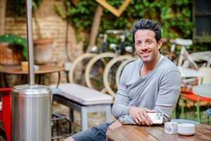 Portrait of a handsome young man sitting at bar table on terrace, looking at camera with a broadly smile 