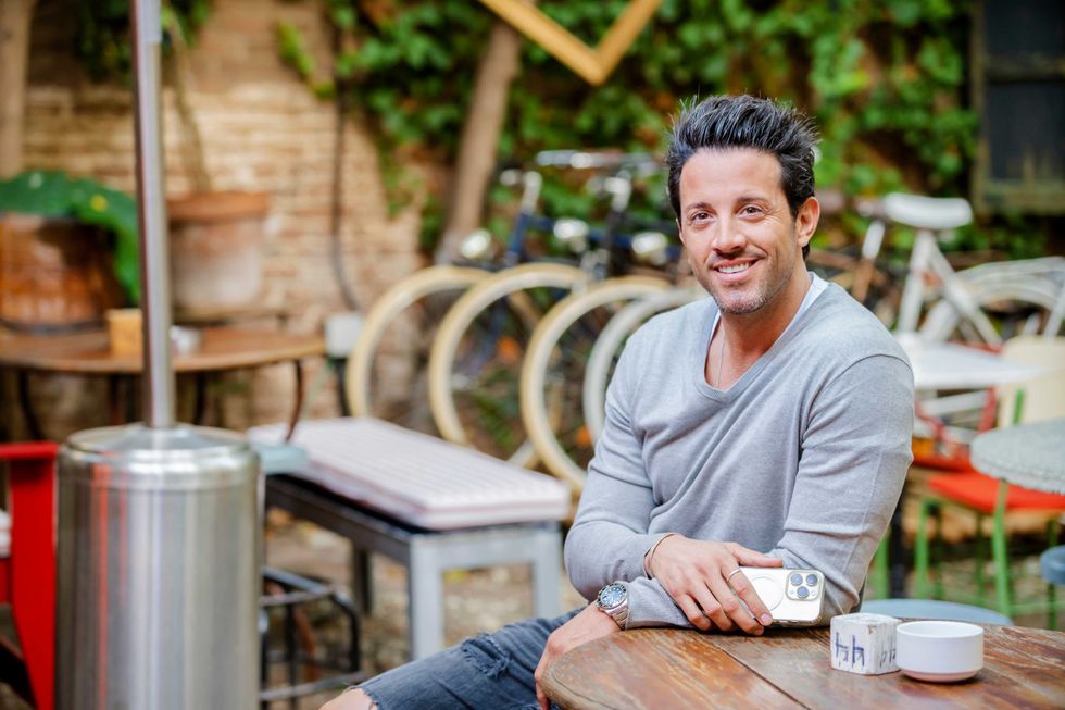 Portrait of a handsome young man sitting at bar table on terrace, looking at camera with a broadly smile