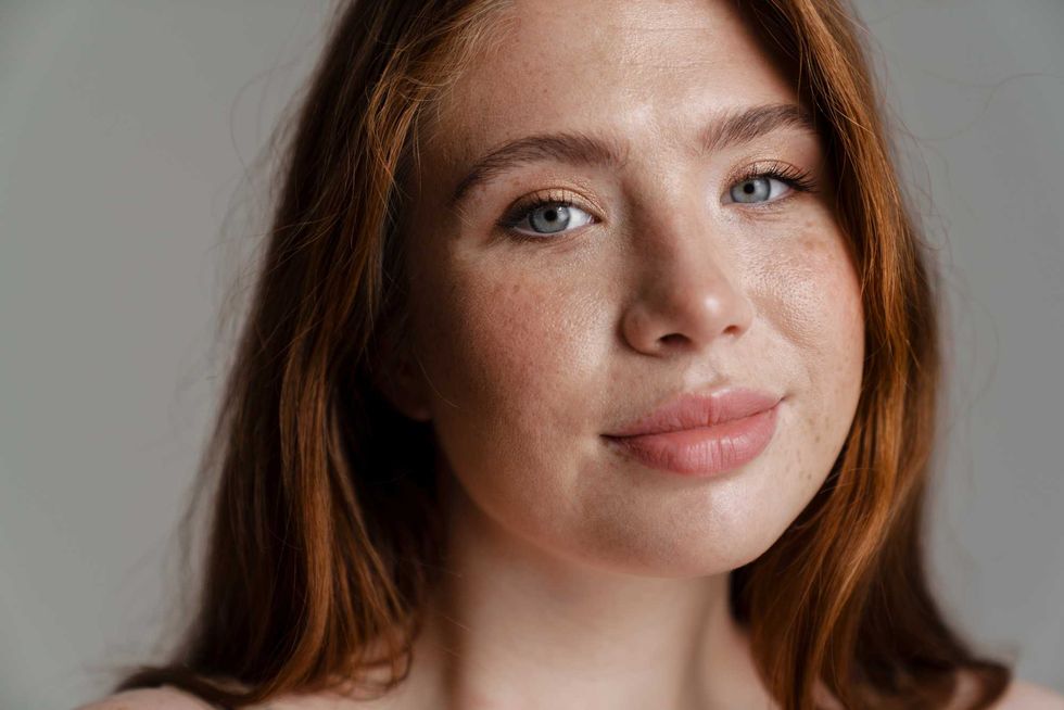 Portrait of a smiling young curvy young white woman with long red hair standing over wall background