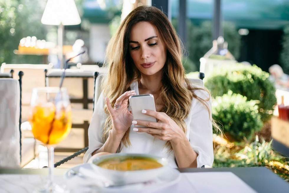 Portrait of attractive young woman sitting in restaurant and using mobile phone