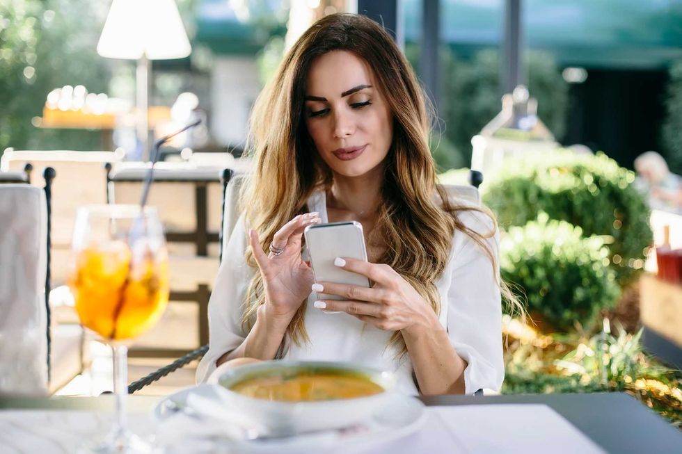 Portrait of attractive young woman sitting in restaurant and using mobile phone