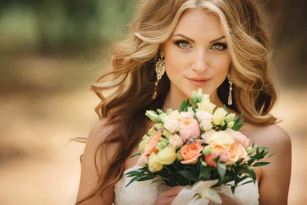 Portrait of beautiful luxury bride with roses wedding bouquet outdoors. Young woman with professional make up and hair style. Wedding day. Marriage