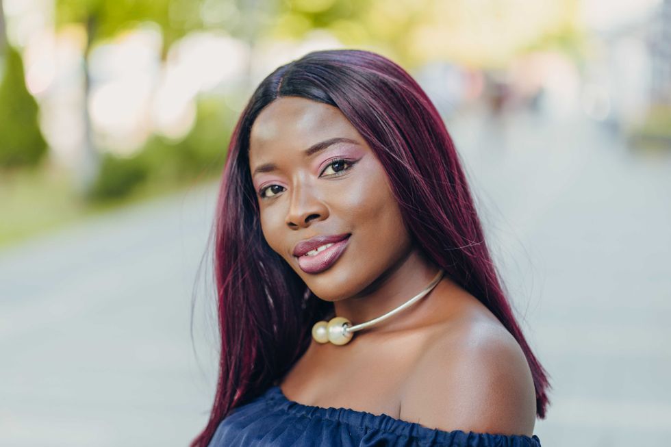 portrait of beautiful young african american woman in blue dress with pink hair hairstyle smiling and walking down the street