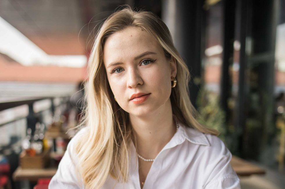 Portrait of beautiful young blonde woman drinking a cup of tea in balcony cafeteria. Happy smiling female relaxing in a coffee shop