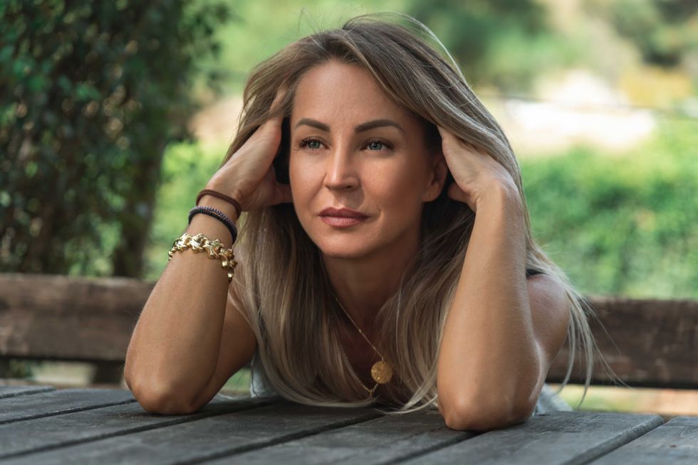 Portrait of happy and tired woman sitting outdoors holding her head with hands.