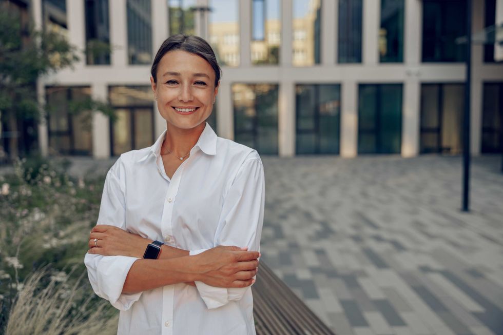 Portrait of smiling female manager standing on modern building background and looks camera