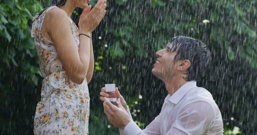 Portrait of young handsome man is making a proposal of marriage to his fiancee under the rain on a background of green trees.