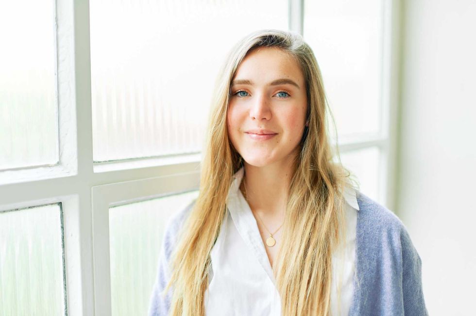 Portrait of young pretty 20 year old girl posing next to big window, looking straight at camera