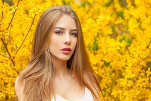 Posing fashion model with long brown hair and natural makeup against floral background outdoor