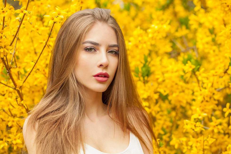 Posing fashion model with long brown hair and natural makeup against floral background outdoor
