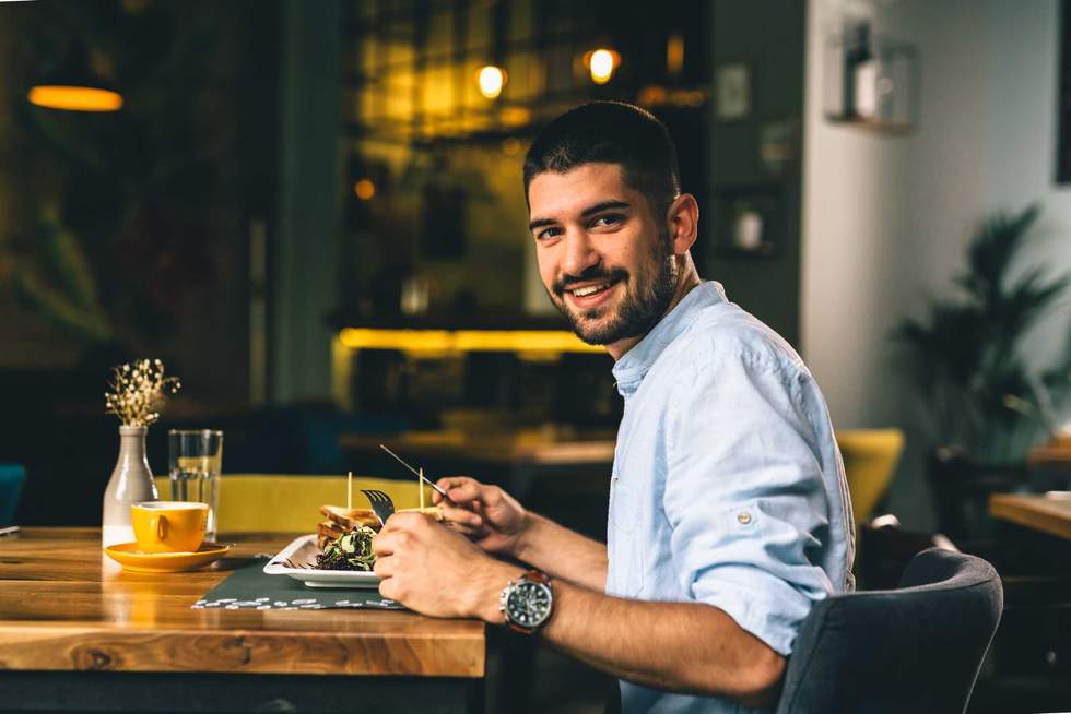 positive young man having breakfast or dinner in cafe
