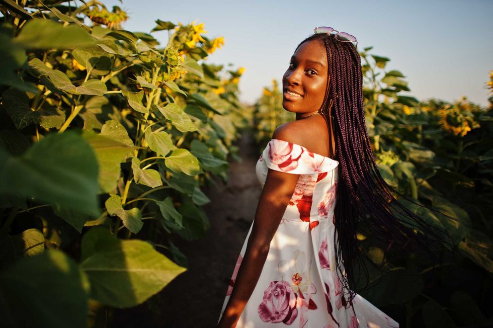 Pretty young black woman wear summer dress pose in a sunflower field.