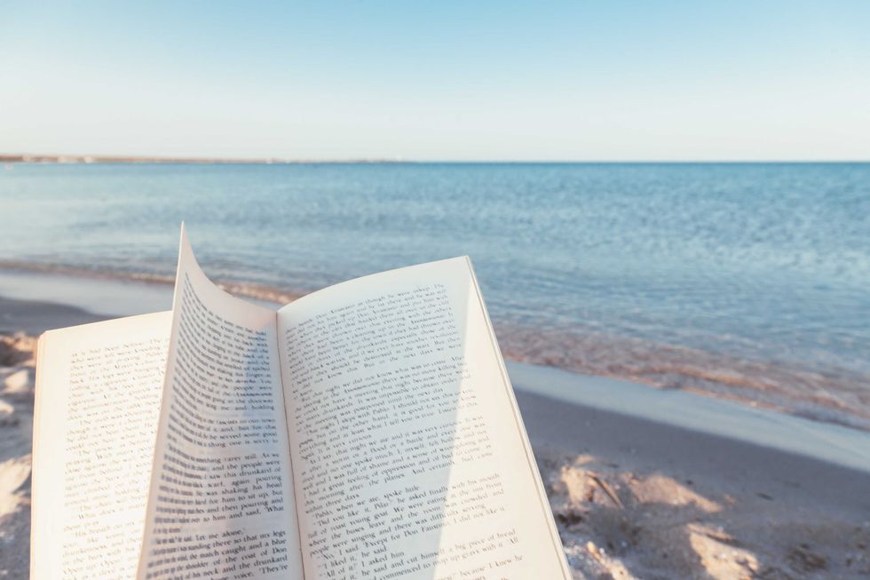 Relax concept. Open book on sand near the sea. Summer vacations still life. The text is transformed and not recognizable.