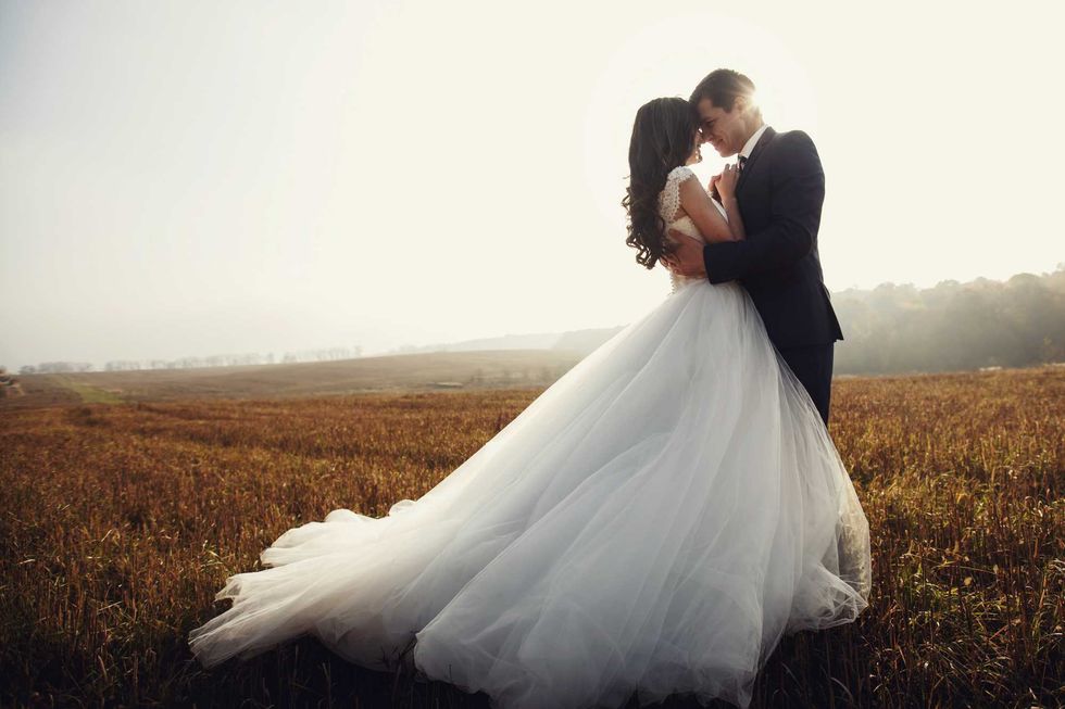 Romantic fairytale newlywed couple hug and kiss in field at sunset