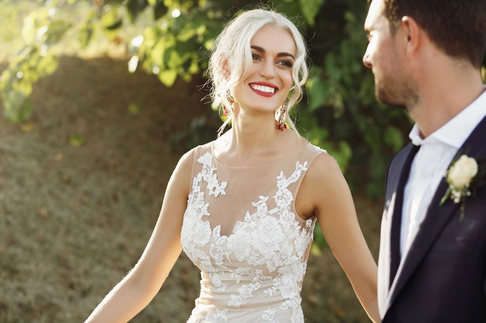 Shiny blonde bride looks at groom with love while they walk outside