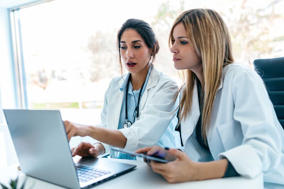Shot of two beautiful female doctors working with her laptop while talking in the medical consultation