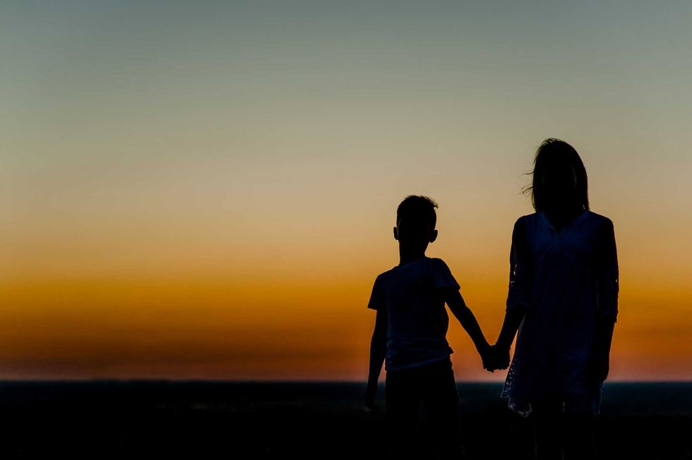 silhouette mother and young boy holding hands at sunset. Space for text.