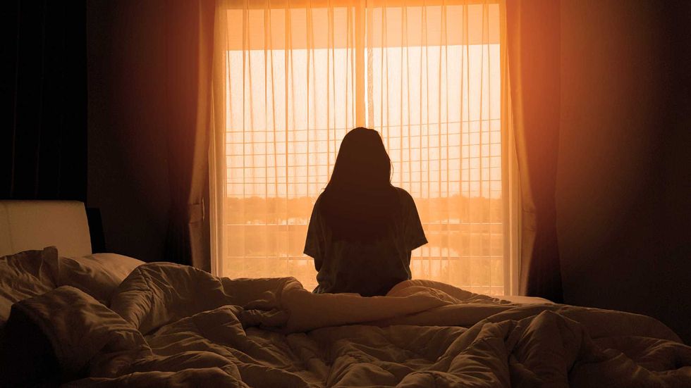silhouette of woman sitting on the bed beside the windows