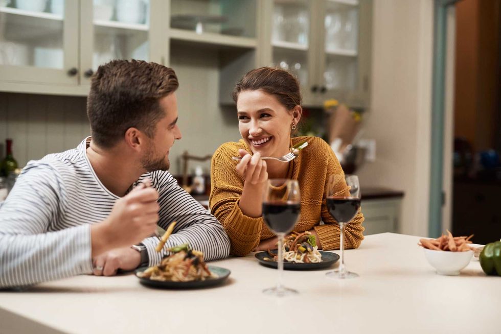 Smile, couple and eating food in home with wine on date night for romance in relationship with bonding. Man, woman and together with dinner or alcohol in kitchen with love, trust and soul connection