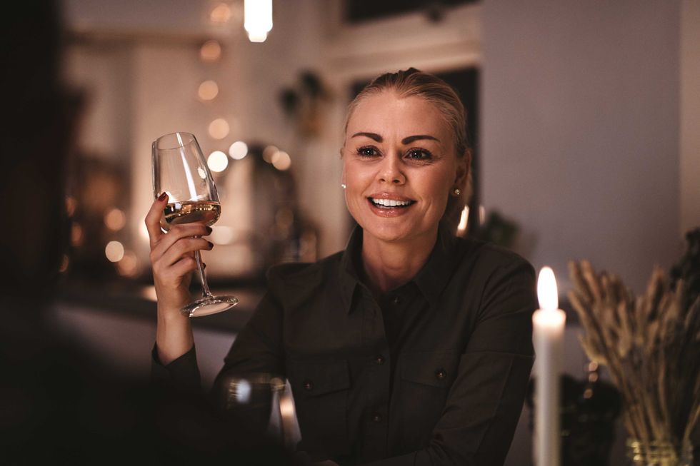 Smiling young woman drinking wine and talking with another guest while sitting at a table during a candlelit dinner party