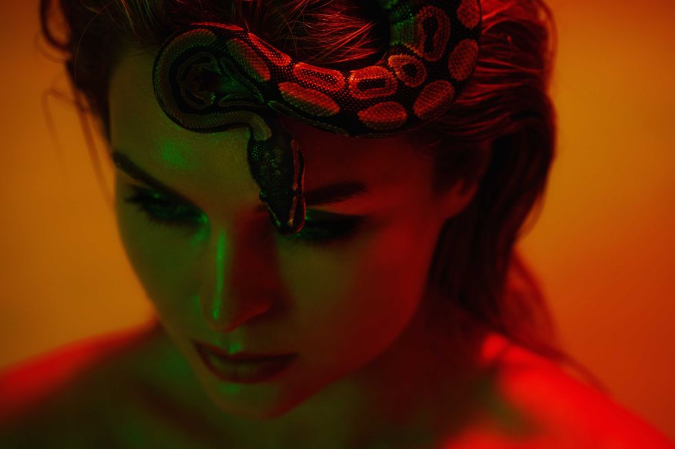 Stunning woman in a mix of red and green light, with a python snake gracefully positioned on her head like a crown.
