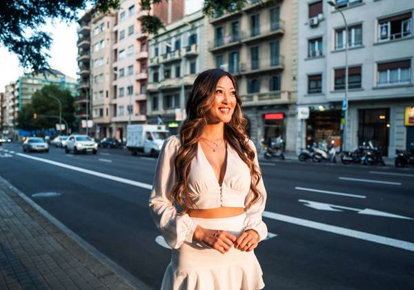Summer sunny lifestyle portrait of young stylish asian girl on the street of big modern city. She wears white dress.