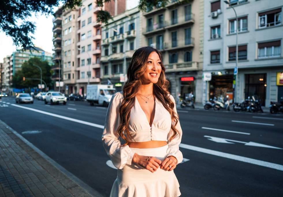 Summer sunny lifestyle portrait of young stylish asian girl on the street of big modern city. She wears white dress.