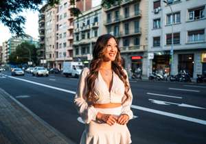 Summer sunny lifestyle portrait of young stylish asian girl on the street of big modern city. She wears white dress.