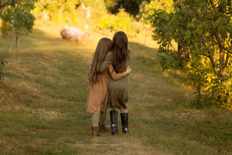 two girls hug on the street in the forest. friendship. in green and brown dress. a park. autum.back view
