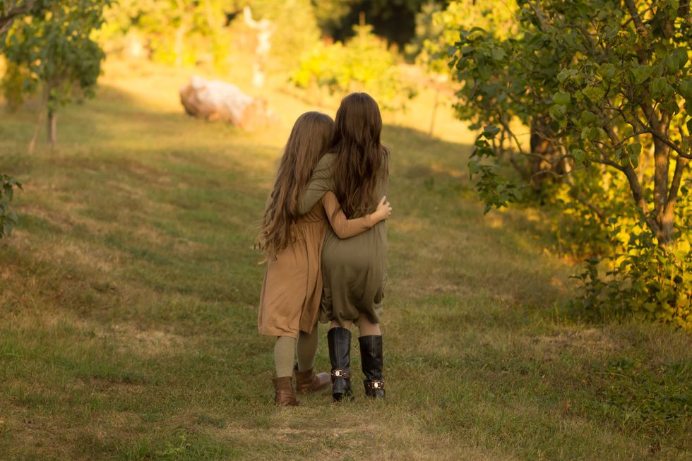 two girls hug on the street in the forest. friendship. in green and brown dress. a park. autum.back view
