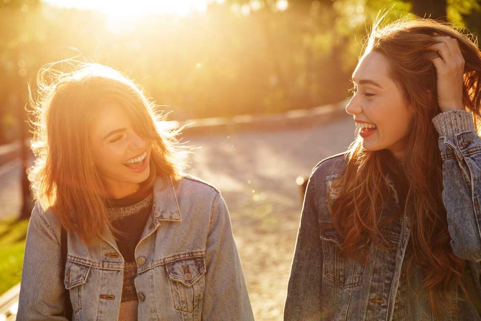 Two happy friends talking and laughing in sunny park