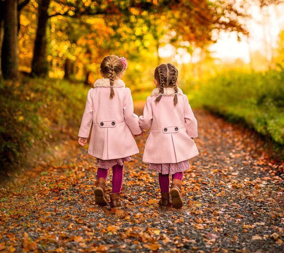 two little girls walking in the woods in pink coats