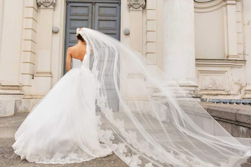 Wedding day. Bride in white wedding dress holding long veil with embroidery