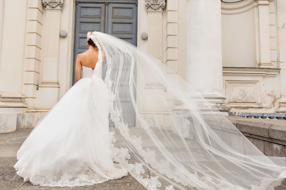 Wedding day. Bride in white wedding dress holding long veil with embroidery