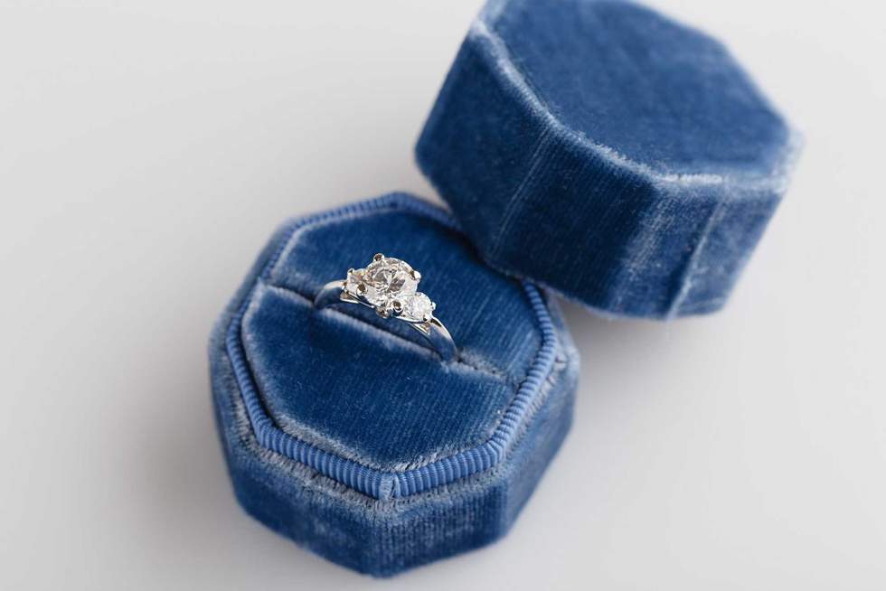 White golden wedding ring with diamonds in blue vintage velvet ring box on white background. Silver engagement ring lifestyle