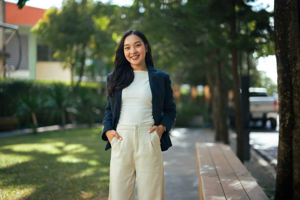 Young Asian woman smiling with hands in pockets standing outdoors in a park
