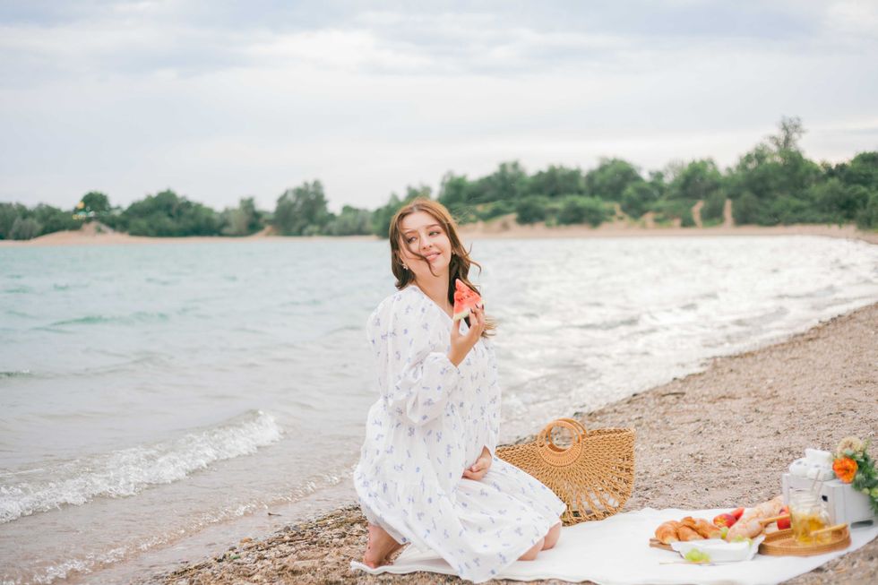 Young beautiful pregnant woman in a beautiful dress near the sea. Picnic. Watermelon. Summer.
