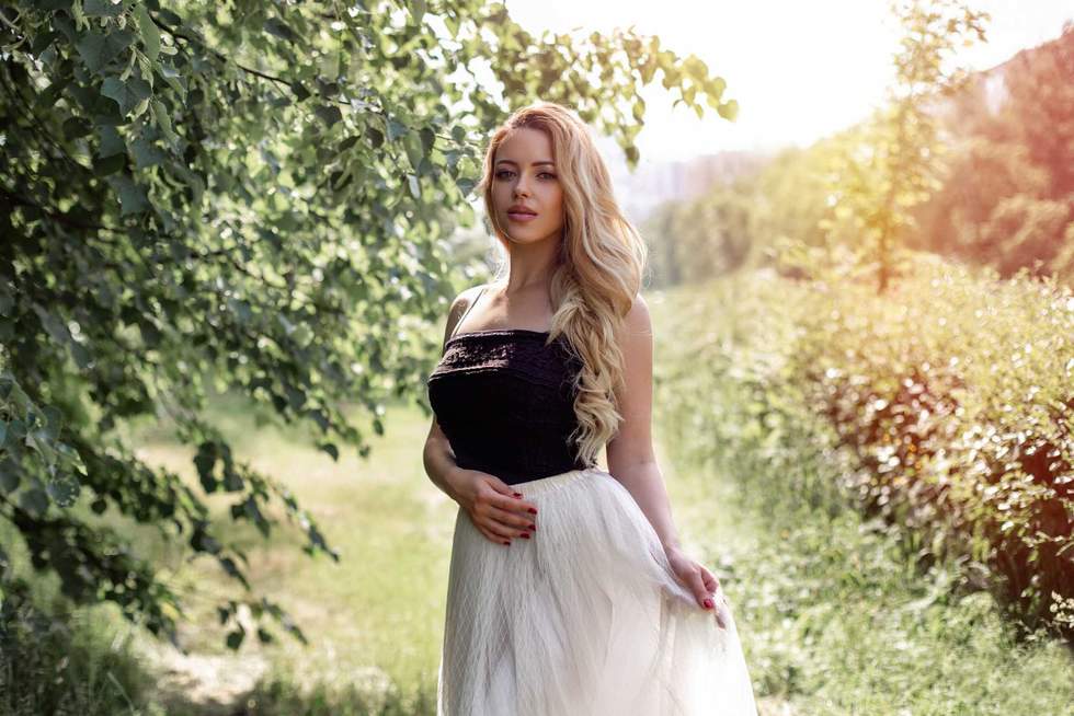 Young beautiful woman with long curly blonde hair and makeup in lace skirt, walking in summer park