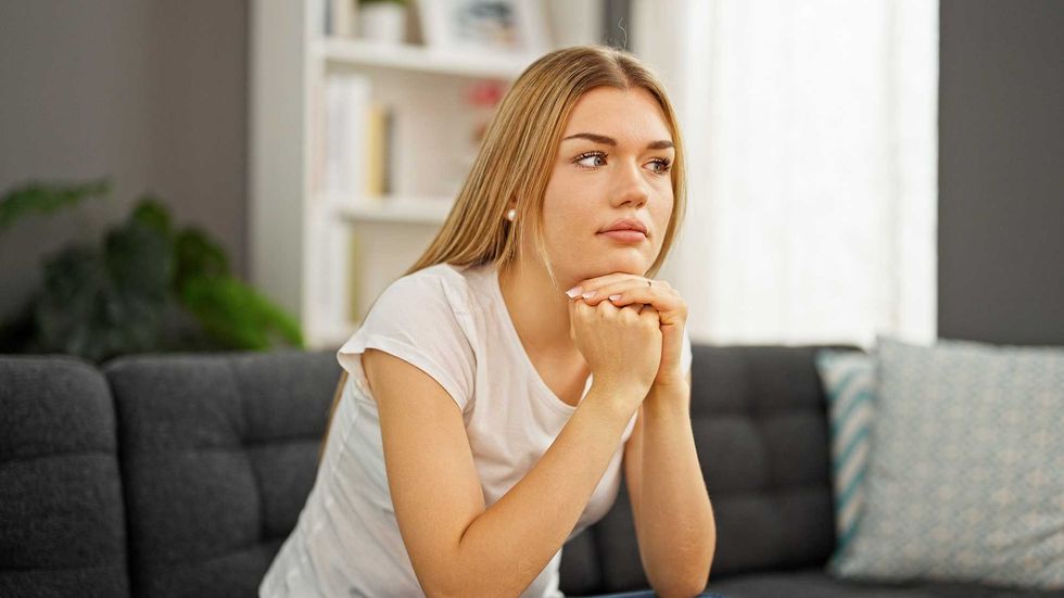 Young blonde woman sitting on sofa with serious expression at home