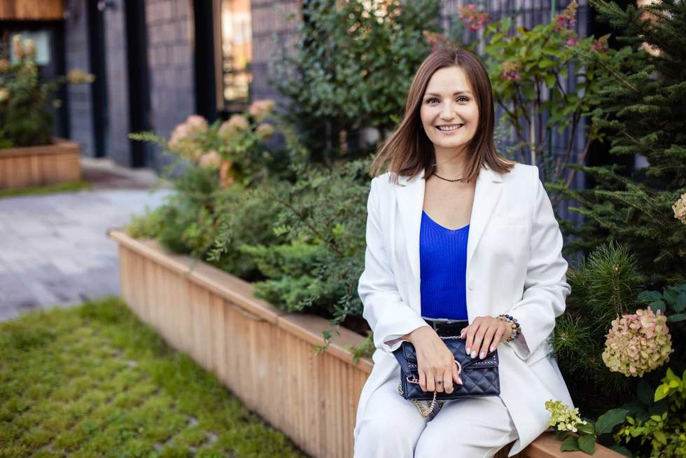Young cute woman sitting on park bench in modern city, smiling and looking at camera.