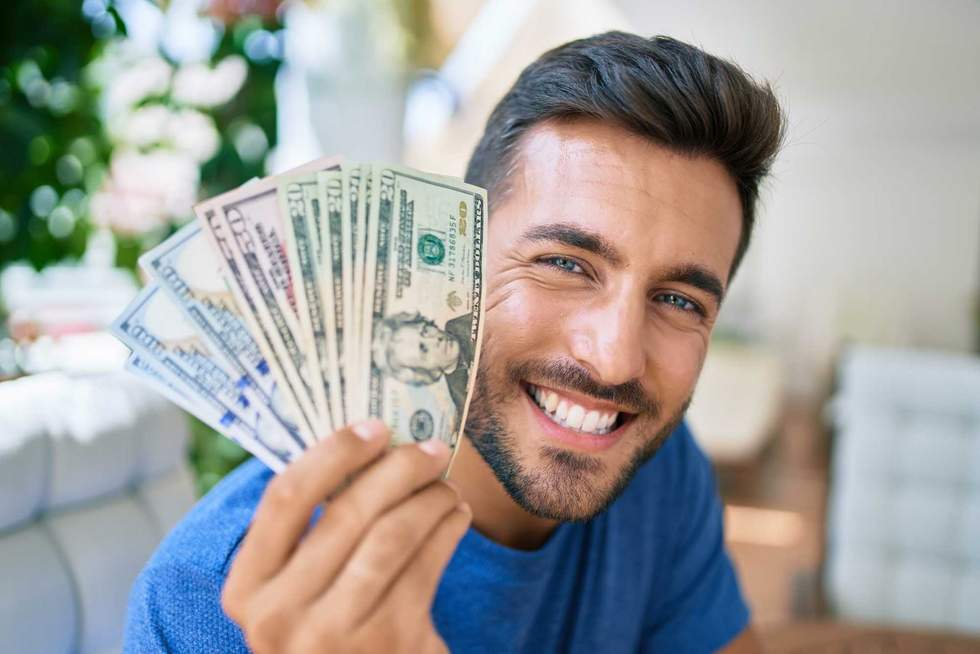 Young hispanic man smiling happy holding american dollars at the terrace.