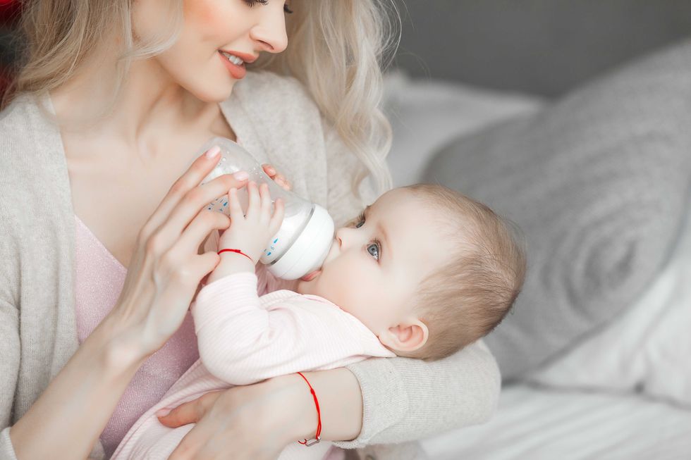 Young mother feeding her little cute baby daughter with bottle of child formula. Woman with her newborn baby at home. Mom taking care of a child. Alternative to breast feeding.
