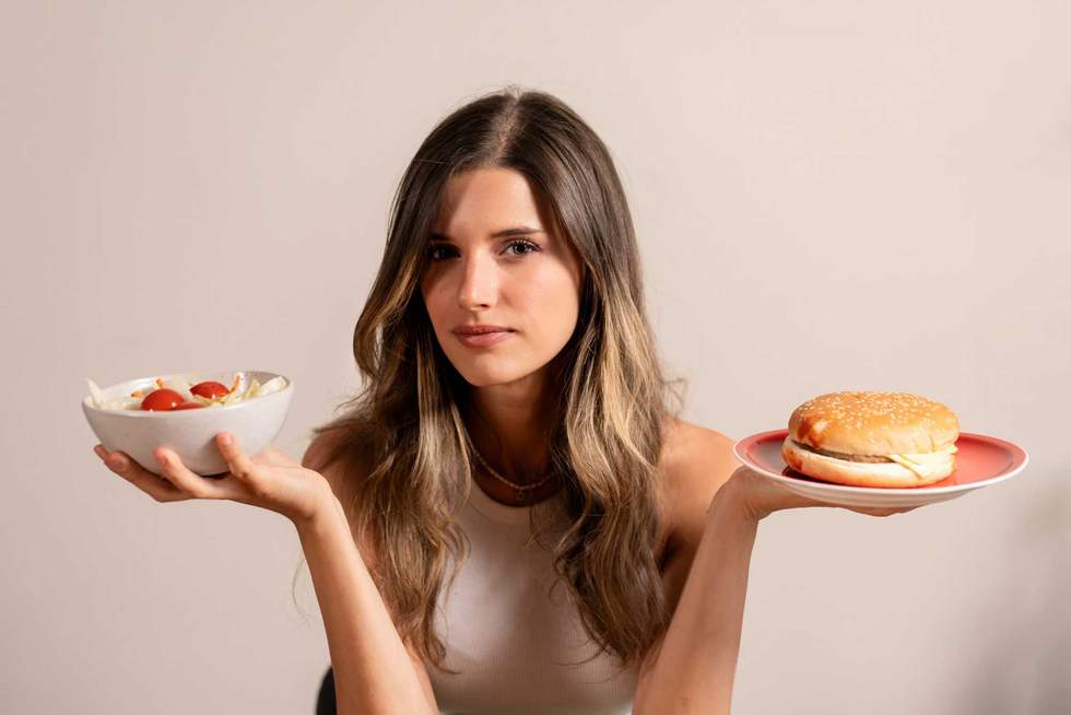Young woman holding healthy salad and hamburger showing food choice dilemma, healthy versus unhealthy eating lifestyle concept