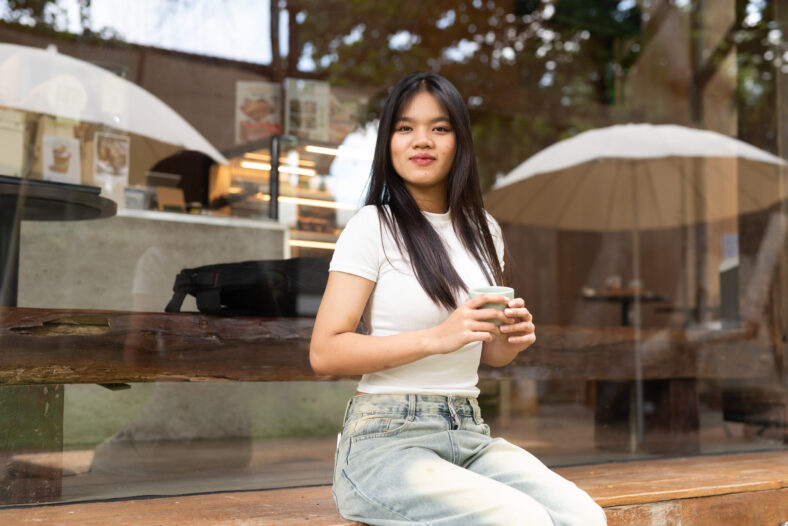 young woman sitting on a bench in the city coffee shop holding mug